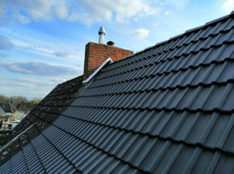 Frisch eingedecktes Steildach mit anthrazitfarbenen Ziegeln und Backstein-Schornstein vor blauem Himmel
