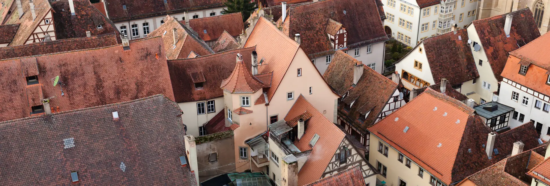 Luftaufnahme einer Ansammlung mittelalterlicher Häuser mit roten Ziegeldächern und Schornsteinen sowie verzierten Giebeln und Fachwerkkonstruktionen.